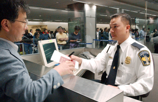 美国申请签证新规定，明年十几种非移民签证免除面谈。图为美国移民检查员Tron Nguyen(右)正在检查一名男子通过海关。(Justin Sullivan/Getty Images)