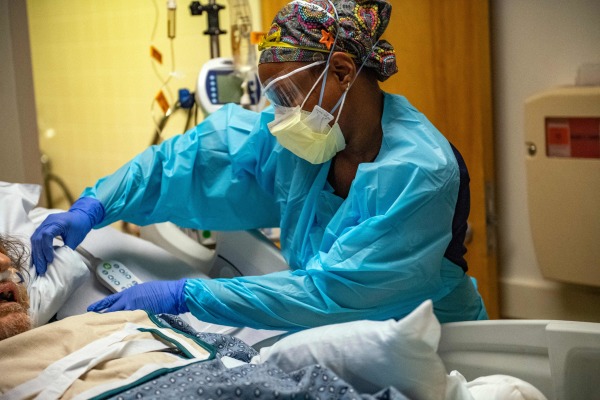 图为2022 年 1 月 4 日，美国马萨诸塞州伍斯特市（Worcester）马萨诸塞大学纪念医疗中心 ICU 病房的一间负压室内，一名身穿全套防护服PPE 的医务人员在为一名新冠病毒感染患者服务。该医院表示他们那里挤满了病人，没有多少床位了。（图片来源：JOSEPH PREZIOSO/AFP via Getty Images）
