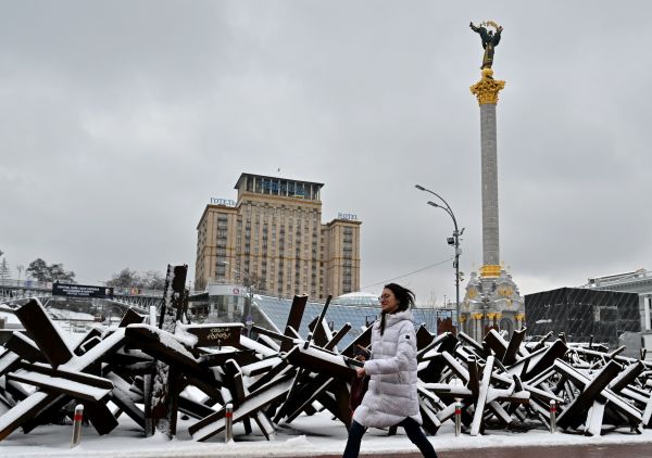 2022 年 12 月 12 日，烏克蘭首都基輔的獨立廣場被白雪覆蓋，一名年輕女子在廣場上部署的反坦克鋼刺猬旁走過。（圖片來源：SERGEI SUPINSKY/AFP via Getty Images）