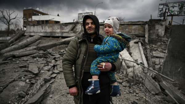 在烏克蘭首都基輔以西的厄平市，一名男子抱著一個孩子站在被炮彈洗劫的斷壁殘垣中。俄羅斯軍隊當天從空中、陸地和海上全面軍事襲擊了烏克蘭的城市，驚恐的平民被迫大規模逃離家園、流離失所。