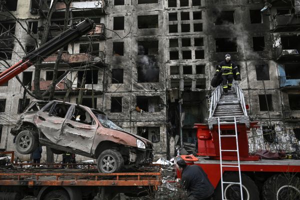 2022 年 3 月 14 日，在烏克蘭首都基輔西北部奧博隆（Obolon）區的一棟公寓樓遭到俄羅斯軍隊的砲擊。砲擊後，有基輔消防員來滅火和查看公寓樓裡的情況。一輛起重機把公寓樓前一輛被砲擊毀壞的小汽車移走。 （圖片來源：ARIS MESSINIS/AFP via Getty Images）