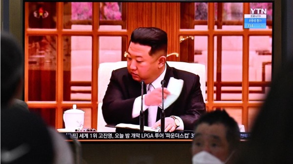 2022年5月12日，人们坐在屏幕旁，看着朝鲜领导人金正恩 (Kim Jong Un) 在电视上摘下口罩，下令在全国范围内进行封锁之新闻广播 
