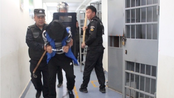 一批被黑客獲取的新疆警察局數據庫文件中的一張圖片，顯示在“再教育營”中警察如何對待被監禁者。（圖片來源：xinjiangpolicefiles.org網站）