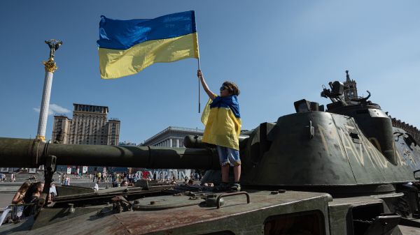 图为2022 年 8 月 21 日，在乌克兰首都基辅市中心，一个小男孩手持一面乌克兰国旗并身裹一面乌克兰国旗站在一辆被缴获的俄罗斯军车上。