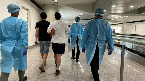 早前向入境處求助的港人抵達香港國際機場。穿上防護裝備的入境處人員協助他們前往專用入境櫃枱辦理出入境手續。（圖片來源：香港政府新聞處）