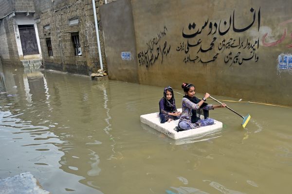 2022年7月26 日，巴基斯坦经卡拉奇暴雨过后，女孩们使用临时木筏穿过住宅区的一条被洪水淹没的街道