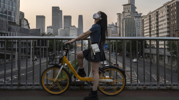 2022年5月31日在北京，一名女子戴着防护口罩停在俯瞰高速公路的人行天桥上。