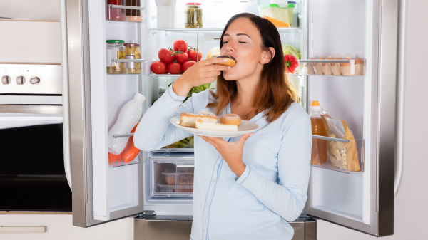 女人站在冰箱前吃东西