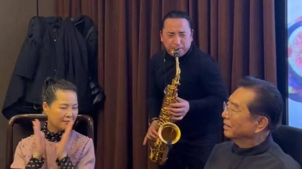 有网友晒出李双江和梦鸽举办酒宴的画面，有乐器表演艺术家还在两个人中间吹奏。（图片来源：网络）