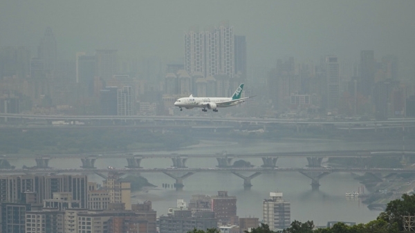 圖為一架飛機 5日午後從淡水河口飛入霧茫茫的台北市區。