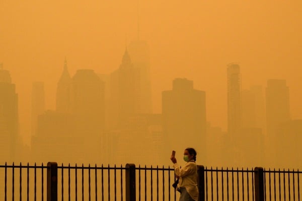 2023 年 6 月 7 日，加拿大野火產生的煙霧導致紐約市出現霧霾，一名戴著口罩的人在拍攝天際線照片。