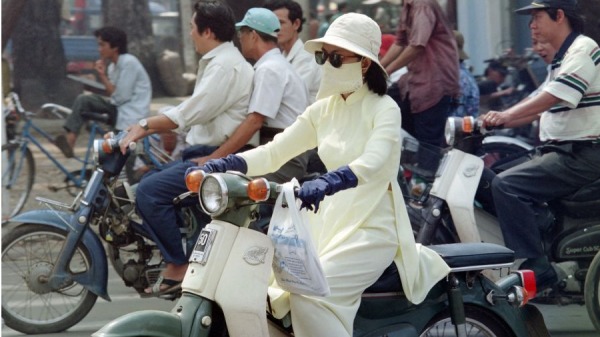 1995年10月21 日，一名妇女蒙着脸骑着摩托车行驶在胡志明市的街道上。
