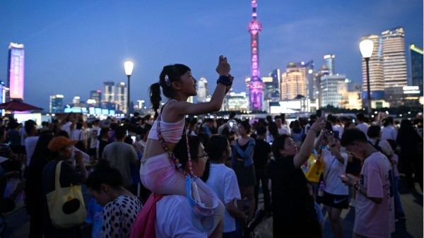 2023年7月5日，一名坐在一名男子肩膀上的孩子在游览上海外滩滨水区时拍照