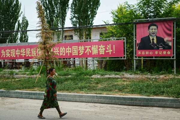 2023年7月16日，一名妇女经过带有习近平的肖像宣传标语前，地点位于中国西北部的新疆地区叶尔羌附近。