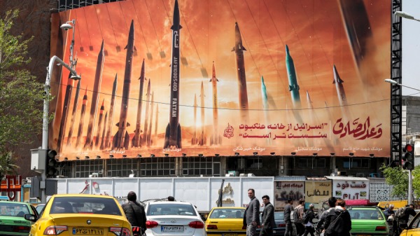 驾驶者驾驶车辆经过一块广告牌，广告牌上描绘了正在服役的伊朗弹道导弹。 