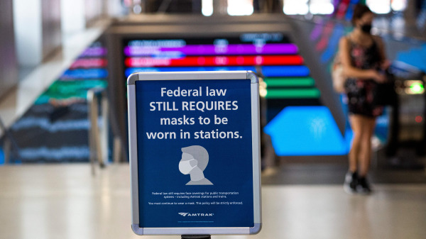一名婦女走過紐約賓夕法尼亞車站的一個要求戴口罩的標誌。