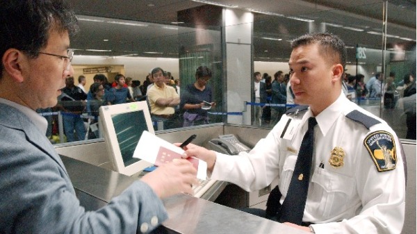 美国申请签证新规定，明年十几种非移民签证免除面谈。图为美国移民检查员Tron Nguyen(右)正在检查一名男子通过海关。(Justin Sullivan/Getty Images)2