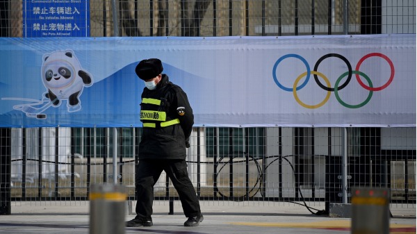 2022年1月18日，在北京冰球比赛场地五棵松体育中心，一名安保人员走过2022年北京冬奥会和奥运五环吉祥物Bing Dwen Dwen的照片。