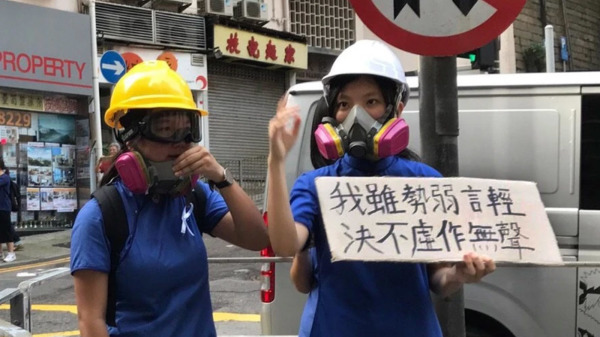 反送中期間，兩名香港女中學生在街頭舉起「我雖勢弱言輕，決不虛作無聲」的紙牌。（圖片來源：立場新聞）