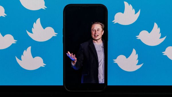 图为2022 年 8 月 5 日拍摄的照片，一部手机屏幕上是美国科技巨富埃隆・马斯克 （Elon Musk）的相片，手机后面的电脑显示器上布满了社交媒体平台推特（Twitter）的小鸟徽标。马斯克于10月27日完成对推特的收购交易，随即迅速对推特进行改造，包括解雇推特三名高管和裁员25%。（图片来源：SAMUEL CORUM/AFP via Getty Images）