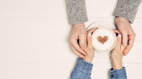 热恋中的情侣手牵手在白色的木桌上喝咖啡。 从上面拍摄的照片，带有复制空间的顶视图 
