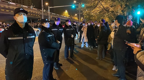 2022年11月28日，北京居民聚集抗议中共清零政策，警方在旁边监督。（MICHAEL ZHANG/AFP via Getty Images）