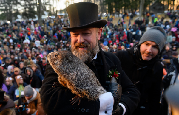 2022年2月2日，美國賓夕法尼亞州的普克蘇托尼（Punxsutawney）小鎮舉行第136屆年度「土撥鼠日」（Groundhog Day）慶祝活動，有5,000多人參加等待日出和土撥鼠露面。圖為土撥鼠管理員德魯姆（AJ Derume）抱著普克蘇托尼小鎮著名的「預言家」土撥鼠「菲爾」（Phil）。日出後，菲爾從他的冬天巢穴中出來，看到了他的影子，這預示者還會有6週惡劣的冬季天氣。如果菲爾沒有看到自己的影子，則預示著會有早春到來。（圖片來源：Jeff Swensen/Getty Images）