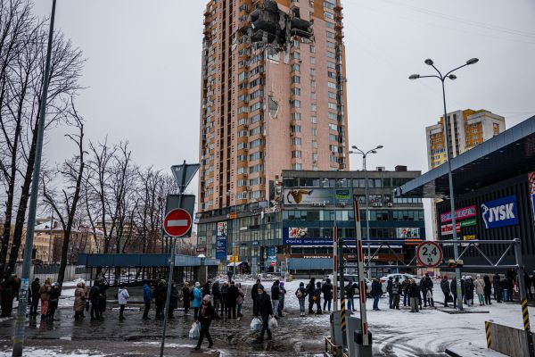2022 年 3 月 1 日，乌克兰首都基辅的市民们在一家超市前排队购买食物，背景是一座受到俄军炮击被局部炸损的建筑物。卫星显示，一支俄罗斯的坦克车队绵延65公里在向基辅扑来。这是俄罗斯入侵乌克兰的第6天。（图片来源：DIMITAR DILKOFF/AFP via Getty Images）