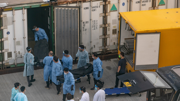 香港第五波新冠病毒疫情死亡人数众多。图为身穿防护衣物的人员，将一具具遗体搬入临时设置用作停尸的冷冻货柜中。（图片来源：Anthony Kwan/Getty Images）