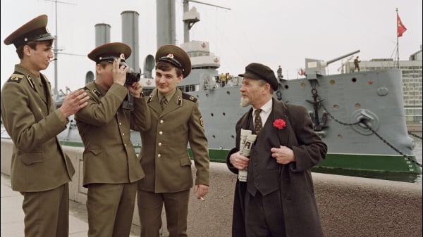 1991年5月3日：一名红军士兵为拿着一份《真理报》的列宁扮演者拍照，他的战友们在旁边开玩笑。背景中是在十月革命政变中发射了一枚礼花空炮的阿芙乐尔号巡洋舰。（图片来源：A. GORELOUSKIAFP via Getty Images）(16:9)