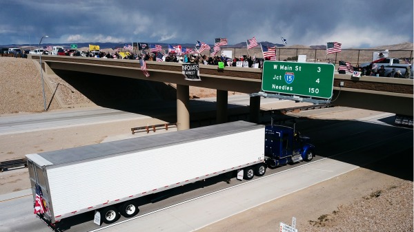 2022年2月23日，当美国人民车队接近加州巴斯托时，当地民众在天桥上挥舞国旗表示支持，他们抗议Covid-19疫苗和戴口罩的强制令。（图片来源：PATRICK T. FALLON/AFP via Getty Images)