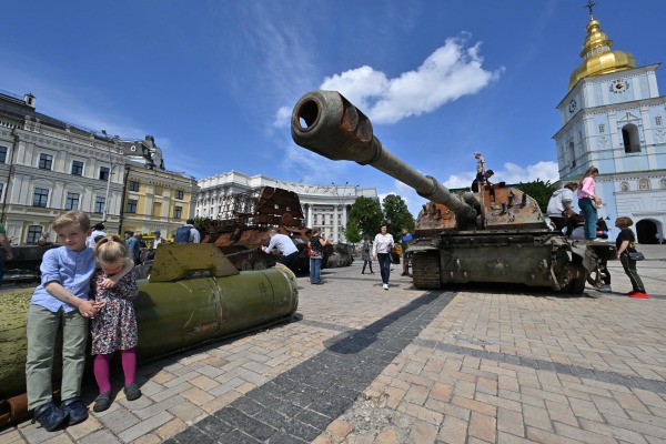 2022 年 6 月 1 日，在乌克兰首都基辅市中心举行的俄罗斯被毁军事装备露天展览会上，两名乌克兰儿童坐在俄罗斯火箭 Tochka-U的残片上，另外还有人在一辆受损的俄罗斯坦克上爬上爬下的观看。此时，俄罗斯入侵乌克兰的战争还在乌克兰东部激烈进行中，俄乌战争到6月3日将满100天。（图片来源：SERGEI SUPINSKY/AFP via Getty Images）