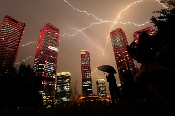 2021 年 6 月 30 日，在北京舉行的中國共產黨成立 100 週年前夕，人們觀看展示燈光秀的建築物時，一道閃電劃過天空。