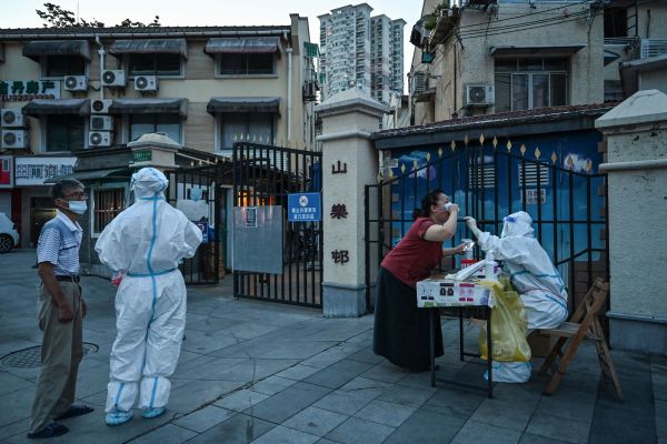 2022年7月5日，一名工作人员在上海静安区居民区旁的街道上对一名妇女进行防疫检测。