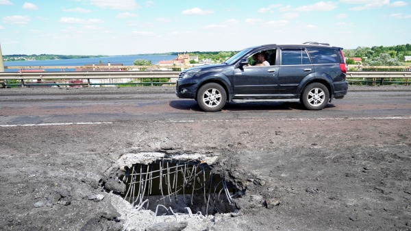 2022年7月21日，一辆汽车驶过第聂伯河对岸的赫尔松安东诺夫斯基桥（Antonovsky bridge），桥上的洞口是乌克兰火箭弹袭击造成的。