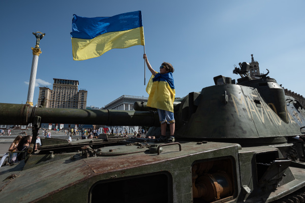 图为2022 年 8 月 21 日，在乌克兰首都基辅市中心，一个小男孩手持一面乌克兰国旗并身裹一面乌克兰国旗站在一辆被缴获的俄罗斯军车上。8月21日是乌克兰国旗日。8 月 24 日是乌克兰于 1991 年宣布脱离前苏联独立后的31周年独立日，也是俄罗斯大规模入侵乌克兰的战争满6个月的日子。（图片来源：Alexey Furman/Getty Images）