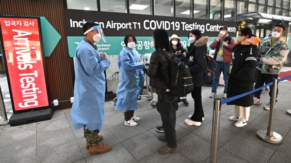 2023 年 1 月 3 日，医护工作人员在首尔仁川国际机场的Covid-19检测中心前指导来自中国的旅客。（图片来源：JUNG YEON-JEAFP via Getty Images）(16:9)