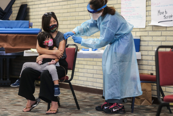 2020年10月14日，在加利福尼亞州萊克伍德當地圖書館舉辦的免費診所，一位母親抱著她的女兒，她們都從護士那裡接種了流感疫苗。