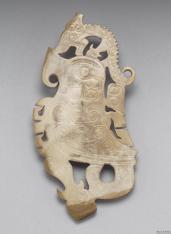 龍冠鳳紋玉飾」以淺浮的雕技法，刻劃出鳳鳥的側面；鳳頭上站著一條龍，龍頭的比例比身體還大。