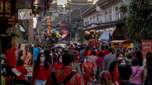 2023年1月21日，曼谷唐人街地区农历新年前夕，穿着红色衣服的人们穿过一条繁忙的街道。