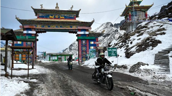 在这张拍摄于2023年4月5日的照片中，摩托车骑手穿过印度东北部阿鲁纳恰尔邦达旺的积雪覆盖的喜马拉雅色拉山口。