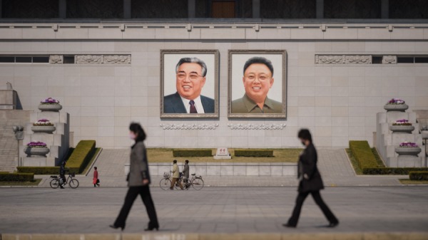 2020年4月9日，朝鮮首都平壤金日成廣場上，戴著口罩的人們走在已故朝鮮領導人金日成和金正日（右）的肖像前