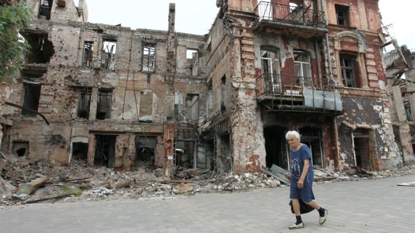 2023年6月10日，乌克兰东南部俄罗斯控制的亚速海港城市马里乌波尔，一名妇女走过一栋被毁的建筑