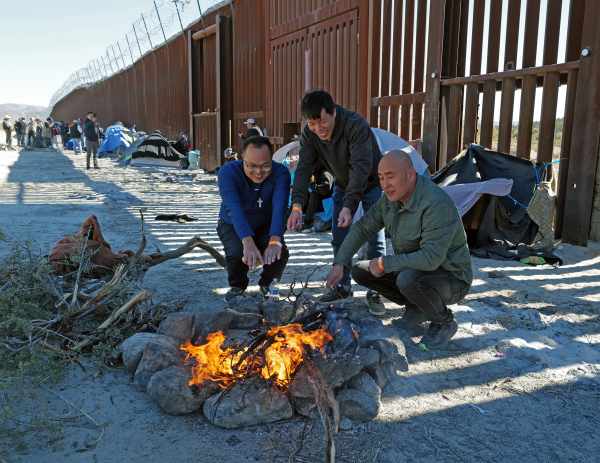 2023年11月12日，試圖從墨西哥進入美國的中國移民被美國海關和邊境保護局拘留，他們坐在火邊取暖。