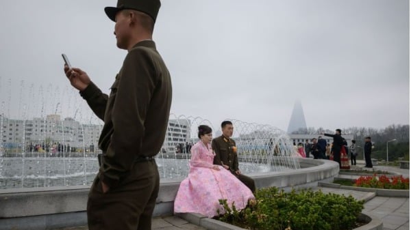 2019年4月18日，平壤一个公园拍摄婚纱照时，一名朝鲜人民军(KPA) 士兵站在新娘和新郎面前看着手机。