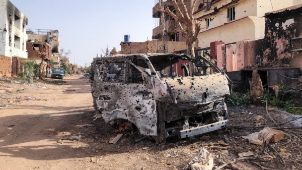 2024年5月30日，显示了恩图曼受损商店前的一辆被烧毁的车辆。苏丹陆军参谋长阿卜杜勒．法塔赫．布尔汉领导的正规军和他的前副手穆罕默德．哈姆丹．达格洛领导的准军事快速支援部队之间的战争已经持续了一年多。