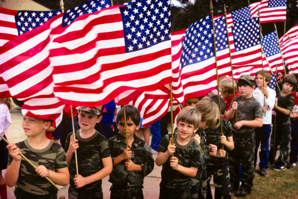 20 世纪 80 年代，一群爱国男孩身着迷彩图案 T 恤，手持美国国旗参加国庆游行。